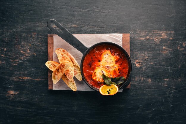 Huevos con tomates y pan tostado en una sartén Shakshuka Vista superior Espacio libre para su texto Sobre un fondo de madera