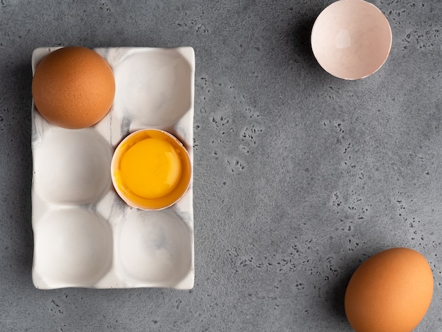 Foto huevos y yema de huevo, cáscara de huevo en soporte de cerámica blanca sobre fondo de hormigón gris. vista superior.