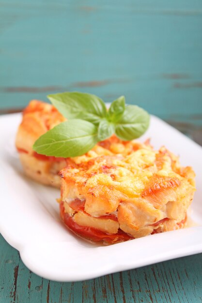 Huhn backte mit Tomaten und Käse in einer weißen Platte auf einem blauen Hintergrund