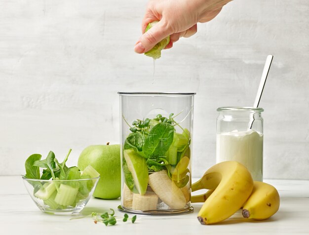 Humane Hand, die Limettensaft in den Mixerbehälter drückt, um einen gesunden Frühstücks-Smoothie auf dem Küchentisch zuzubereiten, selektiver Fokus