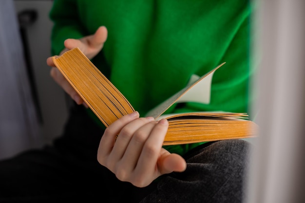 Humano en jeans y un suéter verde sostiene un libro abierto en sus manos. de cerca. foto de alta calidad