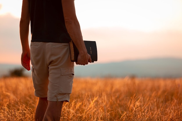 Humano orando na bíblia sagrada em um campo durante o belo pôr do sol.