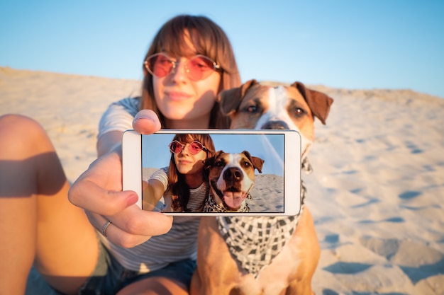 Foto humanos tomando un selfie con perro. concepto de mejores amigos: hembra joven hace autorretrato con su cachorro al aire libre en una playa