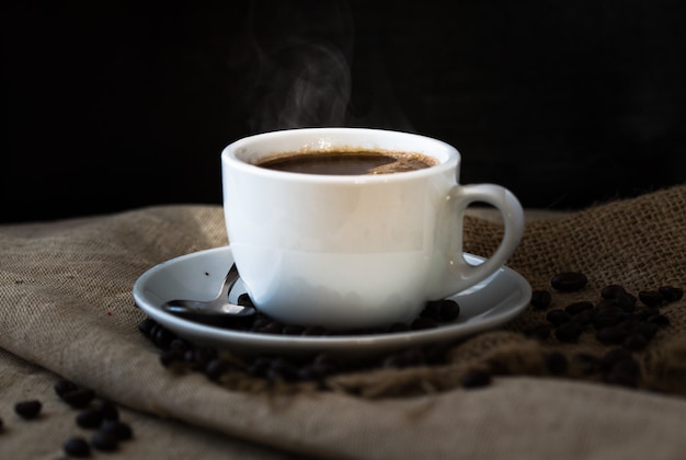 Una humeante taza de café con granos de café en la mesa de madera vintage.