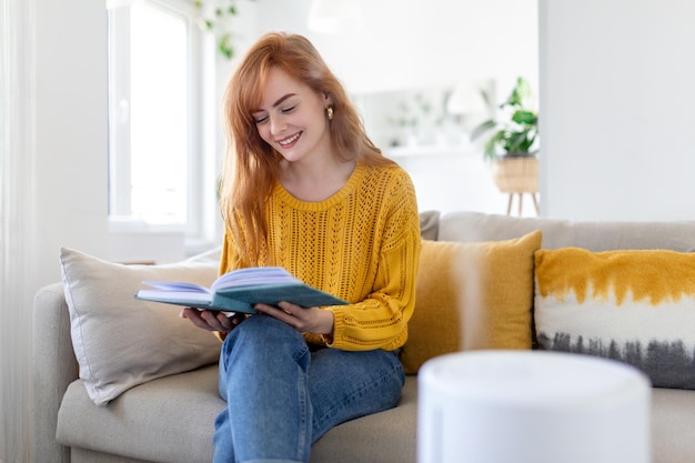 Humidificador de aire moderno y mujer borrosa descansando leyendo un libro en el sofá en el fondo