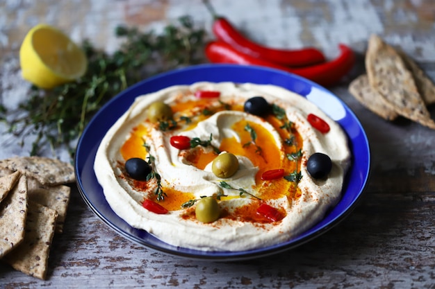 Hummus con aceitunas, pimentón y aceite de oliva en un plato. Plato azul que sirve hummus.