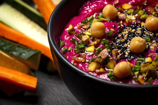 Hummus casero de remolacha y garbanzos con verduras crudas y pan sin levadura sobre fondo oscuro