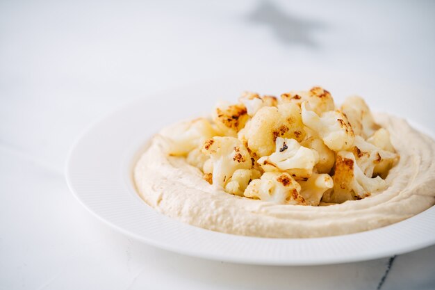 Hummus con coliflor frita sobre mesa de hormigón ligero