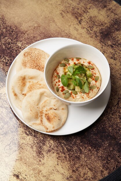 Hummus com abacate e ervas. Prato branco com homus e panquecas na mesa