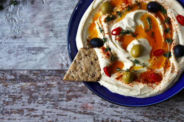 Hummus com azeitonas, pimentão e azeite em um prato. Prato azul servindo hummus.