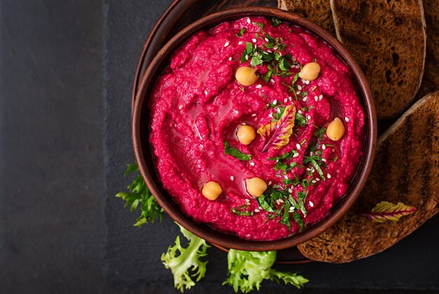 Hummus de beterraba assada com torradas em uma tigela de cerâmica em uma mesa escura