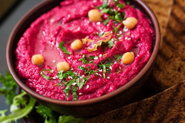 Hummus de beterraba assada com torradas em uma tigela de cerâmica em uma mesa escura