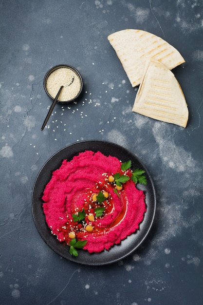 Hummus de beterraba caseiro em um prato de cerâmica preta sobre concreto escuro