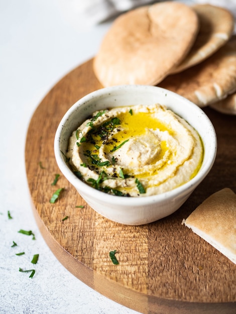 Hummus de ervilha de grão de bico caseiro tradicional, regado com azeite de oliva e salsa fresca e fatias de pita frescas na tábua de madeira