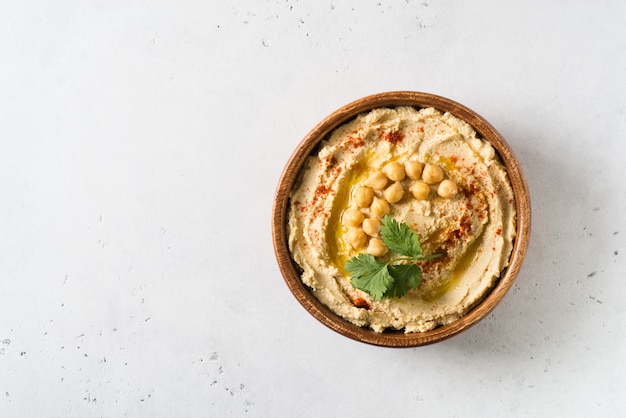 Hummus dip con garbanzo y perejil en placa de madera sobre fondo blanco