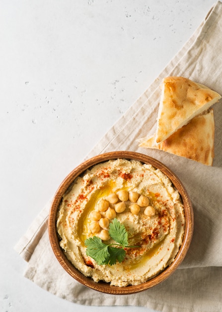 Hummus dip con garbanzo, pita y perejil en placa de madera sobre fondo blanco