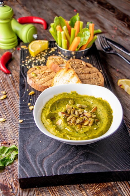 Hummus con espinacas, aguacate y semillas de calabaza en un bol sobre una tabla de madera y bruschetta