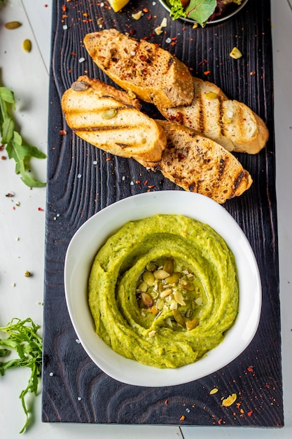 Hummus con espinacas y semillas de calabaza en un bol sobre una tabla de madera cocina oriental