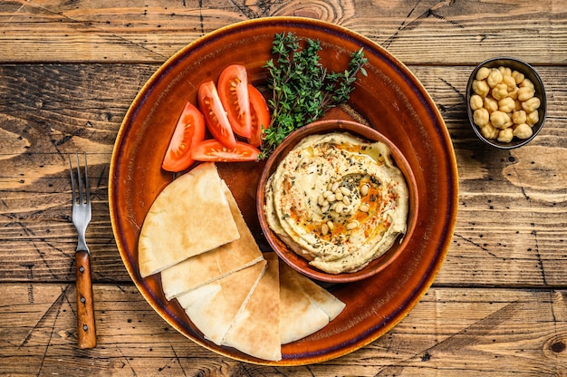 Hummus fresco com pão pita, tomate e salsa em um prato rústico.