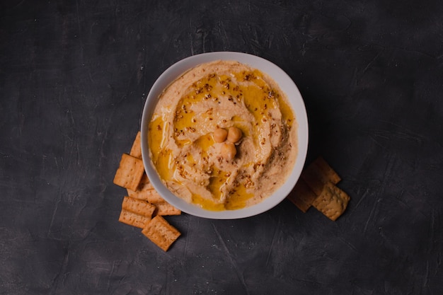 Hummus de garbanzos con aceite de oliva y sésamo tostado sobre fondo oscuro y enfoque selectivo