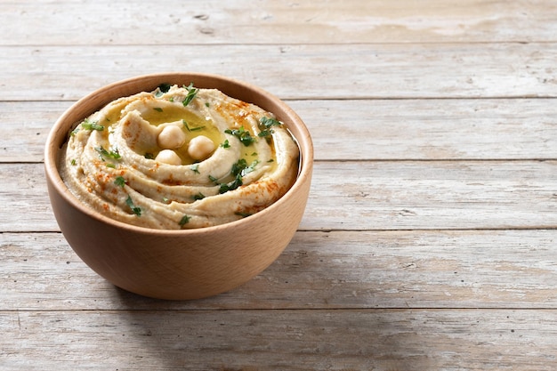 Hummus de garbanzos en un cuenco de madera adornado con pimentón de perejil y aceite de oliva en la mesa de madera