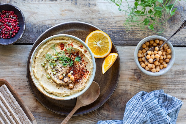Hummus, Kichererbsensauce mit geräuchertem Paprika-Olivenöl in einer Keramikschale auf einem hölzernen Hintergrund. Draufsicht.