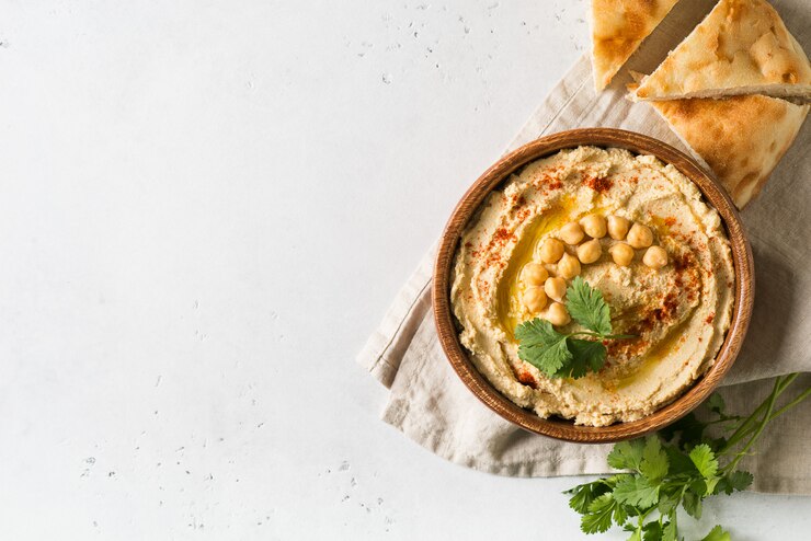 Hummus mergulho com grão de bico, pita e salsa em placa de madeira no fundo branco