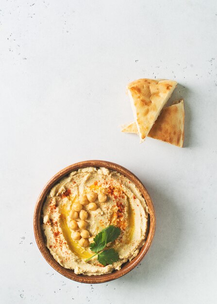 Hummus mergulho com grão de bico, pita e salsa em placa de madeira no fundo branco