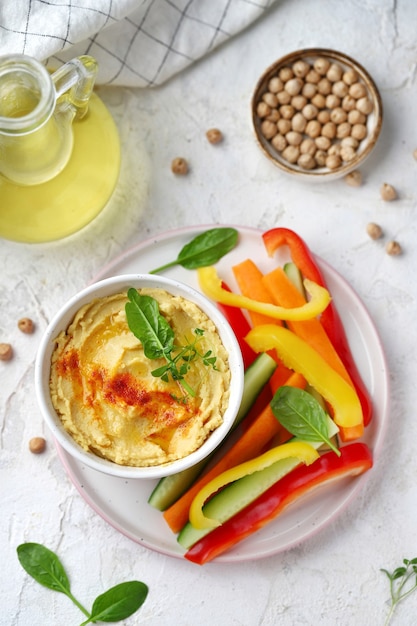 Hummus mit frischem Gemüse und Grün auf einem weißen Teller und Hintergrund