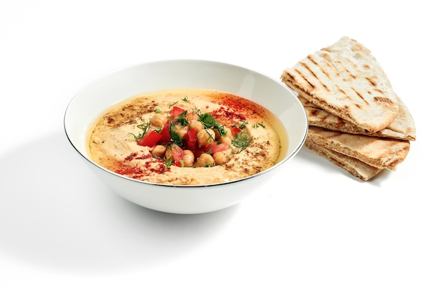 Hummus mit Gewürzen, Kichererbsen, Tomaten und Fladenbrot in einer Schüssel isoliert auf weißem Hintergrund