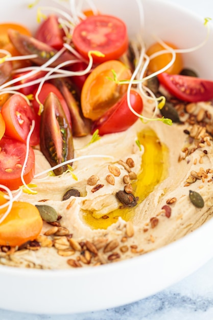 Hummus mit Tomatenkeimlingen, Nüssen und Olivenöl auf weißem Teller mit weißem Marmorhintergrund