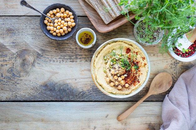 Hummus, molho de grão de bico com azeite de páprica defumado em uma tigela de cerâmica em um fundo de madeira. Vista do topo. Copie o espaço.