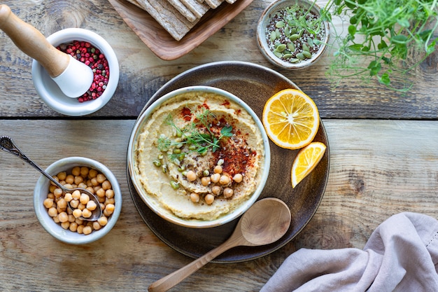 Hummus, salsa de garbanzos con aceite de oliva pimentón ahumado en un recipiente de cerámica sobre un fondo de madera. Vista superior.