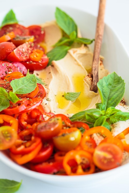 Foto hummus con tomates pimientos albahaca y aceite de oliva en plato blanco fondo blanco