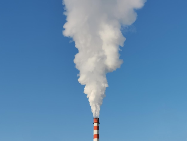 Humo blanco de una chimenea roja y blanca de una fábrica contra un cielo azul brillante. Contaminación ambiental. Concepto de protección de la ecología y la naturaleza.