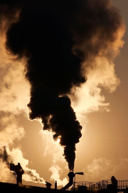 El humo que emite una tubería industrial contra el cielo al atardecer