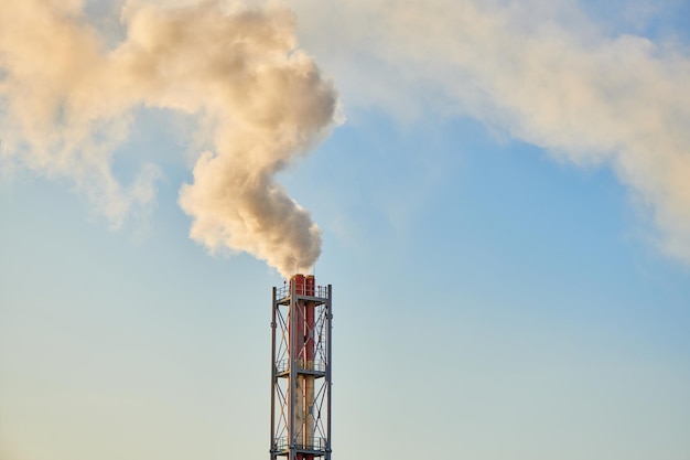 Humo que sale de la chimenea. Enorme humo de la pipa. Chimenea roja-blanca de fábrica. Contaminación ambiental. Emisiones de dióxido de carbono. Concepto de protección del clima global.