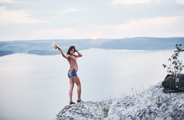 Foto humor do pôr do sol. garota atraente turista posando na borda de uma montanha com um lago de águas claras no fundo.