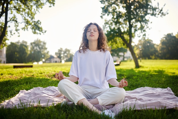 Humor meditativo. Uma garota de branco meditando no parque e parecendo em paz