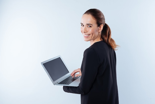 Humor positivo. Alegre mujer joven agradable volviéndose hacia usted y sonriendo mientras sostiene su netbook