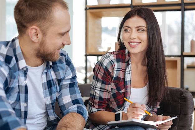 Humor positivo. mulher bonita e atraente alegre sorrindo e olhando para a colega enquanto escreve algo no caderno