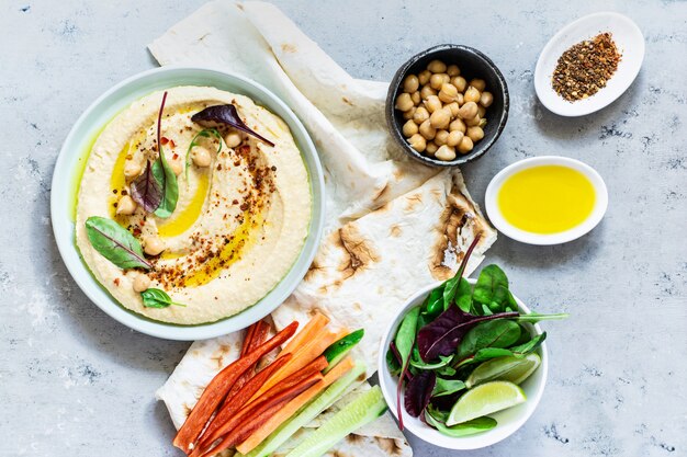 Humus clássico em uma tigela com ervas, páprica defumada, azeite e alface em um fundo azul (cinza). Comida vegetariana saudável.