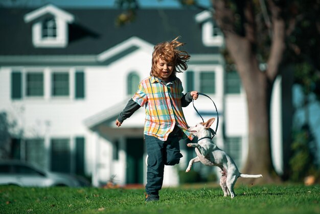 Hund mit Leine, der mit kleinem Jungen des Handlers auf einem Hintergrund des grünen Hinterhofrasens in einem Sommer läuft