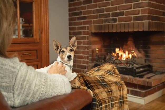 Hund sitzt im Winter auf einer Frau vor dem gemütlichen Kaminfeuer
