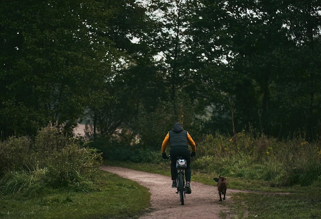 Hund und Fahrrad Rückansicht eines Mannes, der Fahrrad fährt, während sein Hund in seiner Nähe läuft