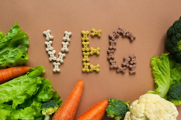 Hund vegetarische trockene Crunchies in Form von Knochen mit Gemüse auf beiger Oberfläche. Schriftzug VEG.