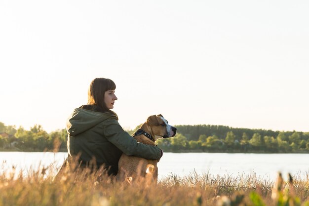 Hundebesitzerin und ihr Haustier sitzen am Flussufer bei Sonnenuntergang