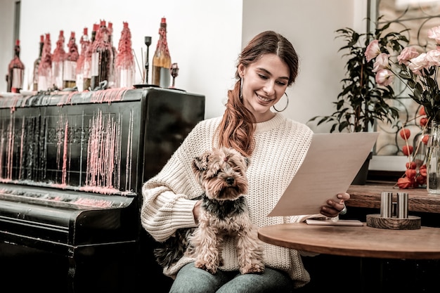 Hundefreundliches Restaurant Frau, die das Menü im Café liest, während sie ihren Hund hält