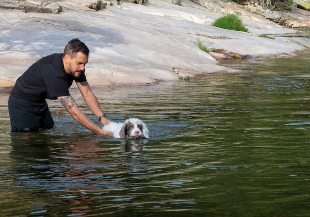 Hundeführer, der dem Welpen beibringt, in der Lagune zu schwimmen. Weißer Welpe, der in einem See schwimmen lernt.