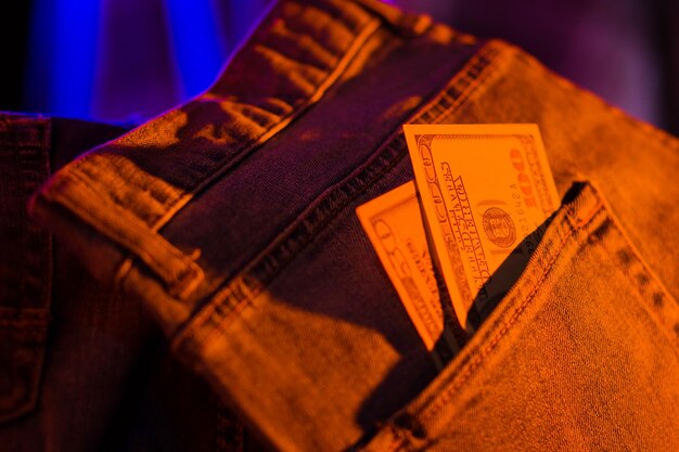 Hundertdollar-Schein in der Tasche einer blauen Jeans, Dollar im Neonlicht, Banknoten.